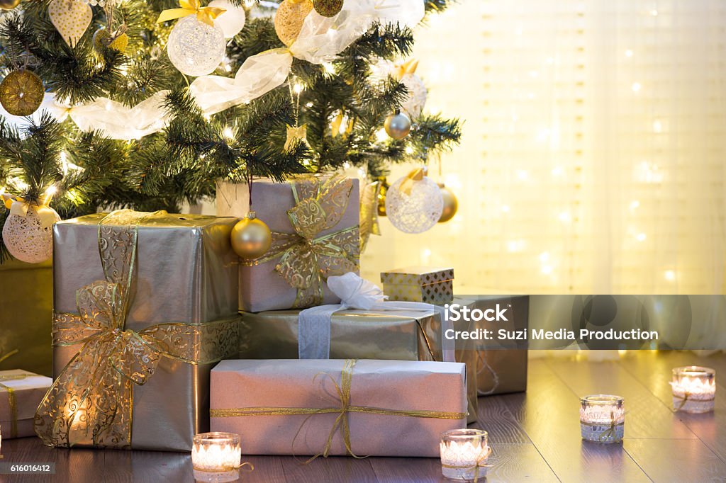 Christmas background Tall christmas tree, beautifully decorated with balls, bows and lights. Lots of christmas gifts under the tree. Candles on wooden floor. Christmas Tree Stock Photo