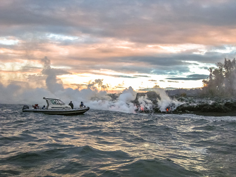 Big Island, Hawaii, United States - August 7, 2010: Sunrise lava boat tour Hawaii. Tourists on a speedboat, observed during a tour, the lava of Kilauea Volcano as it enters the Pacific Ocean.