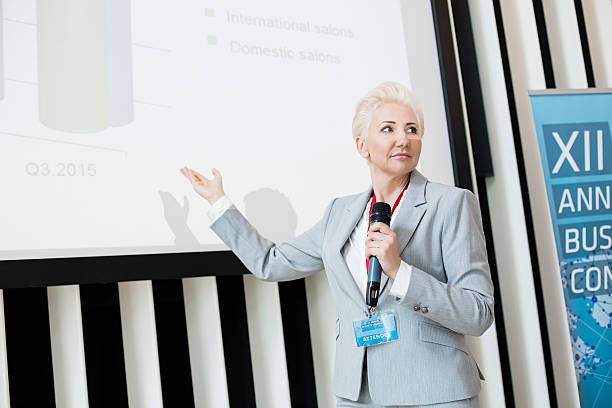 istock Businesswoman explaining strategy on projection screen at convention center 616021228