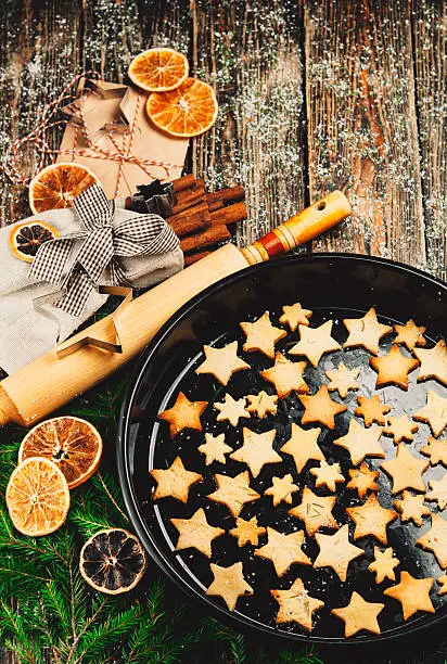 Christmas Gingerbread. Form for baking., fir branches, dried oranges, a wooden rolling pin, cinnamon sticks in bag on wooden background.Cookies in the form of stars on the baking sheet.
