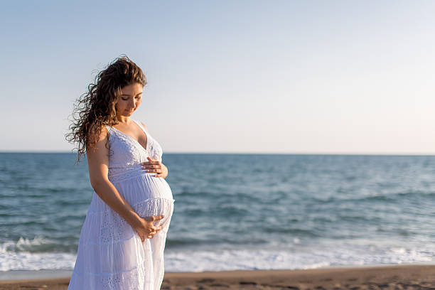 istock Young pregnant woman walking on the beach 616093638