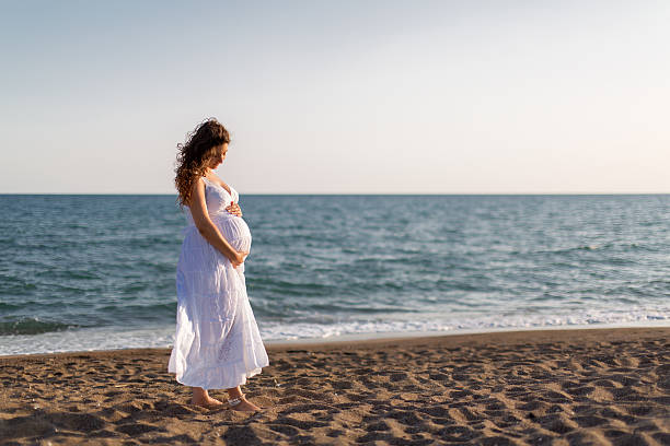 istock Young pregnant woman walking on the beach 616093726
