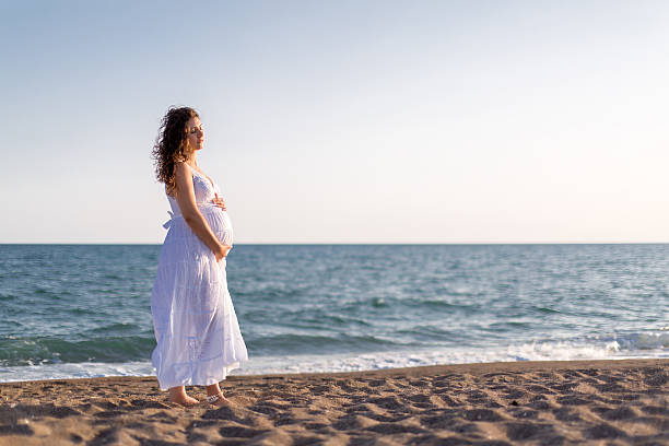 istock Young pregnant woman walking on the beach 616093936