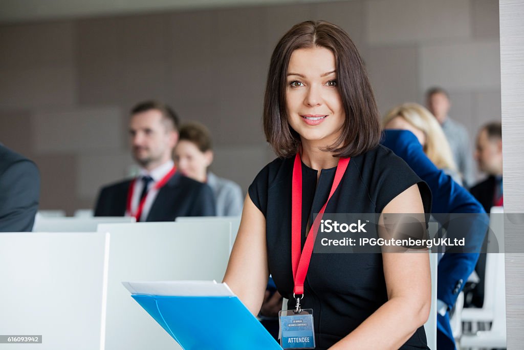 Portrait of confident businesswoman sitting in seminar hall Lanyard Stock Photo