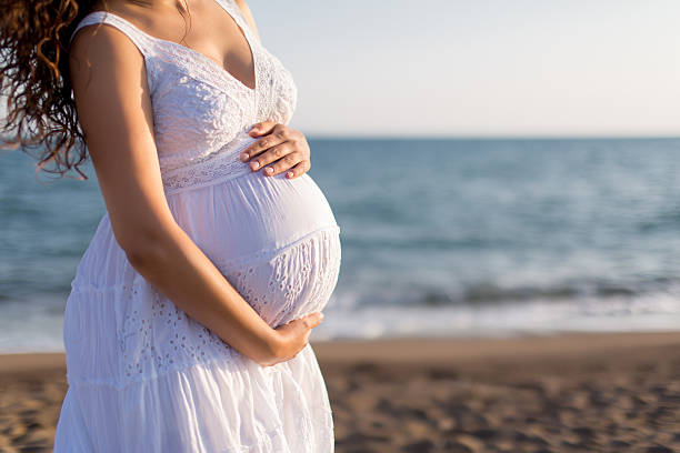 istock Young pregnant woman walking on the beach 616094032