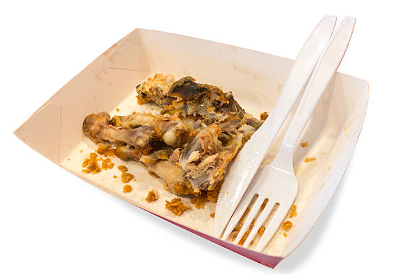 Food waste on paper plates with plastic knives and forks isolated white background. The file includes a clipping path so it is easy to work.
