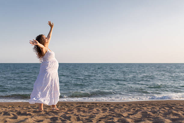 istock Young pregnant woman walking on the beach 616094342