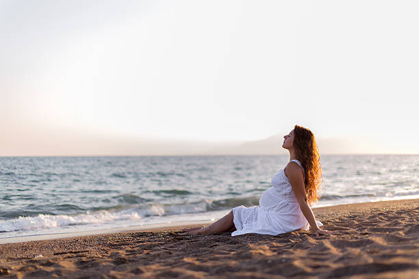 istock Young pregnant woman walking on the beach 616095556