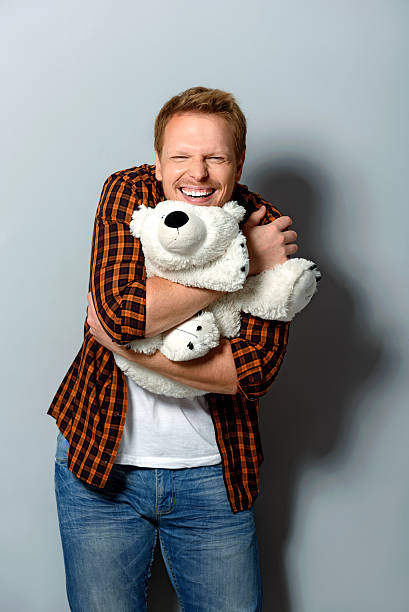 happy male hugging a toy smiling adult person looking into camera while holding big teddy bear man with teddy bear stock pictures, royalty-free photos & images