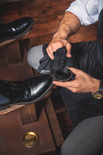 hands of a guy polishing the shoes craftsman applying wax with a rag on a pair of boots, close up shoe polish photos stock pictures, royalty-free photos & images