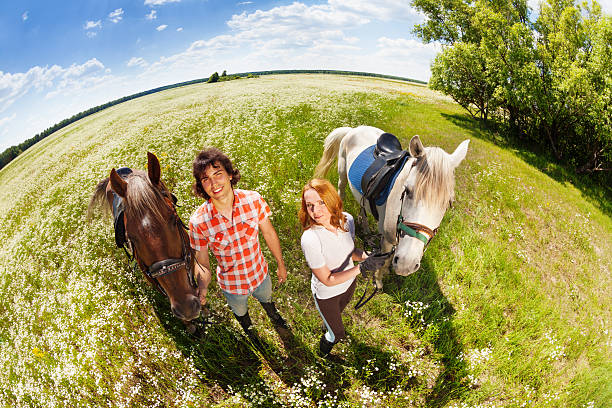 Top view portrait of young happy couple walking with their purebred horses in flowery meadow