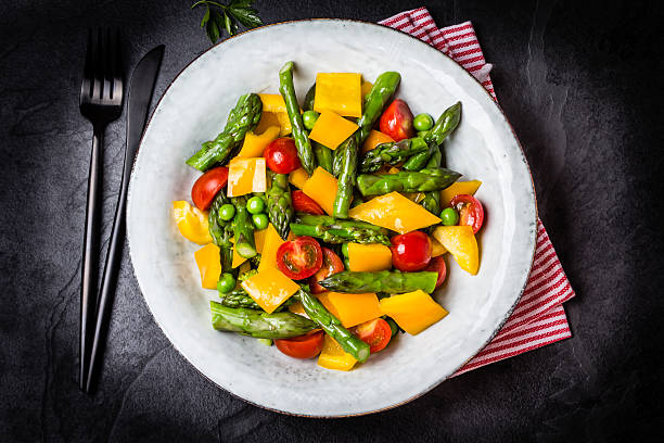 Vegetarian salad with asparagus, cherry tomatoes, bell pepper, slate background Mediterranean vegetarian salad. Vegan salad with asparagus, cherry tomatoes, yellow bell pepper on gray plate on black slate stone background. Vegetarian or healthy food. Top view asparagus organic dinner close to stock pictures, royalty-free photos & images