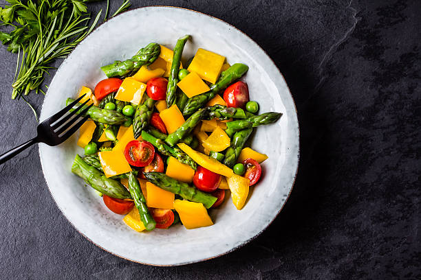 Vegetarian salad with asparagus, cherry tomatoes, bell pepper, slate background Mediterranean vegetarian salad. Vegan salad with asparagus, cherry tomatoes, yellow bell pepper on gray plate on black slate stone background. Vegetarian or healthy food. Top view asparagus organic dinner close to stock pictures, royalty-free photos & images