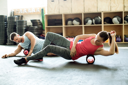 Young man and woman doing pilates on support roller at modern gym