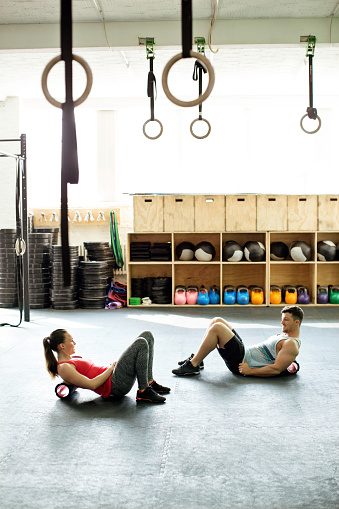 Young man and woman exercising with foam roller on gym floor