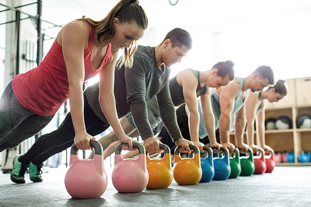 Gym class doing push-ups on kettlebells Group of young men and women doing push-ups on kettlebells in a gym kettlebell stock pictures, royalty-free photos & images