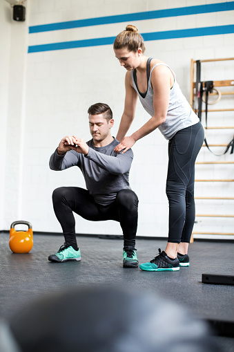 Full length shot of female personal trainer guiding man doing exercising at gym