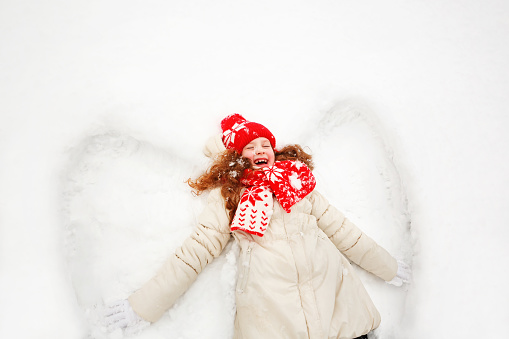 Laughing girl laying on a snow moving her hand up and down, playing winter outdoors.