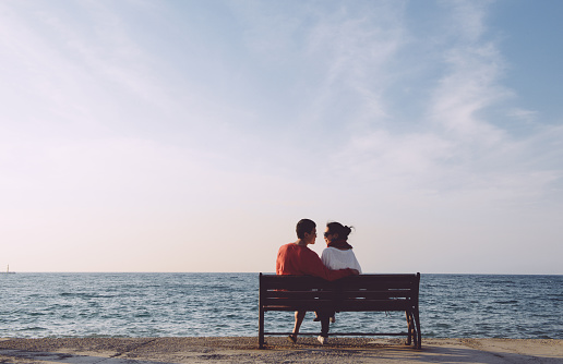 back portrait of young couple looking at each other on bench by the sea in Kusadas, Turkey, clean composition