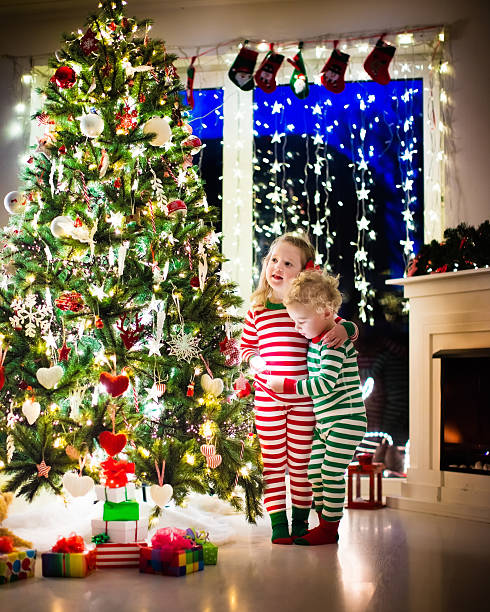 istock Kids in pajamas under Christmas tree next to fire place 616132692