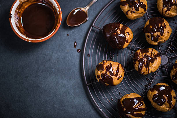 profiteroles эклеры опираясь на охлаждение стойки - профитроль стоковые фото и изображения