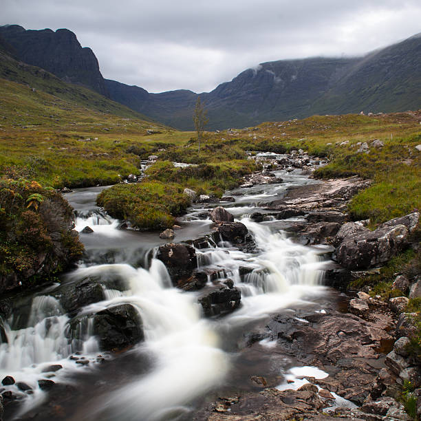 Sgurr a' Chaorachain and the Russel Burn The Russel Burn mountain stream tumbles over rocky waterfalls in a valley below Sgurr a' Chaorachain mountain, beside the Bealach na Ba mountain pass in the north west Highlands of Scotland. applecross peninsula stock pictures, royalty-free photos & images