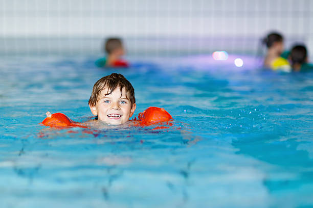 istock kid boy with swimmies learning to swim in indoor pool 616229540