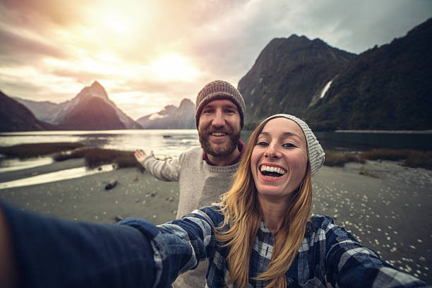 Mitre peak selfie at Milford sound, New Zealand Cheering young couple take a selfie portrait in front of the Mitre peak in Milford sound, New Zealand. mitre peak stock pictures, royalty-free photos & images