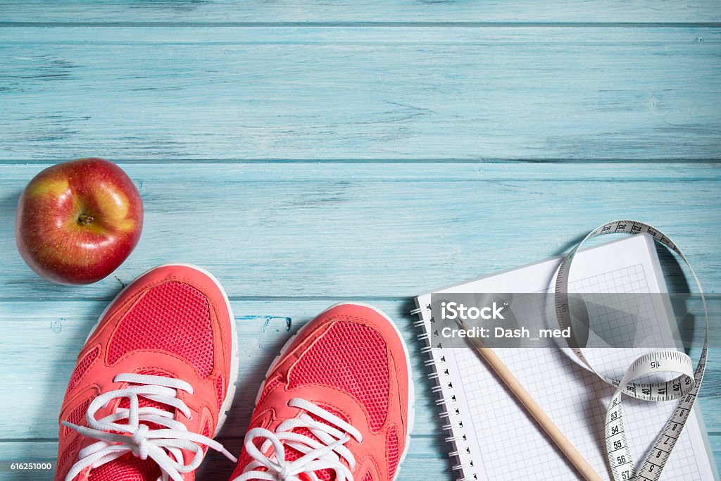 Fitness concept, pink sneakers, apple and notebook and measuring tape Fitness concept, pink sneakers, red apple and notebook with pencil and measuring tape on wooden background, top view Healthy Lifestyle Stock Photo
