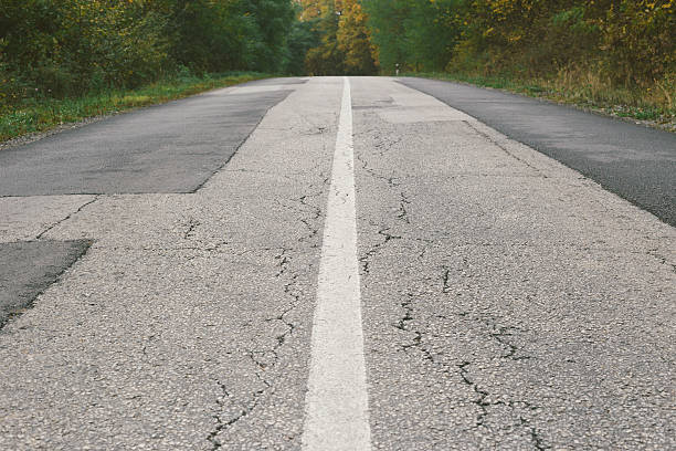 Dividing line on old cracked and patched asphalt road. Photo is taken with dslr camera outdoors in autumn.