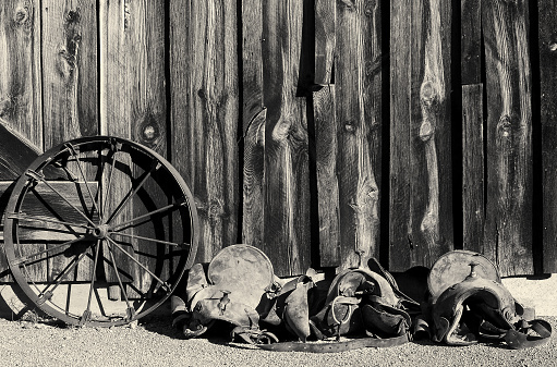 Black and white vintage Wild West photo of horse saddle and metal wagon wheel 