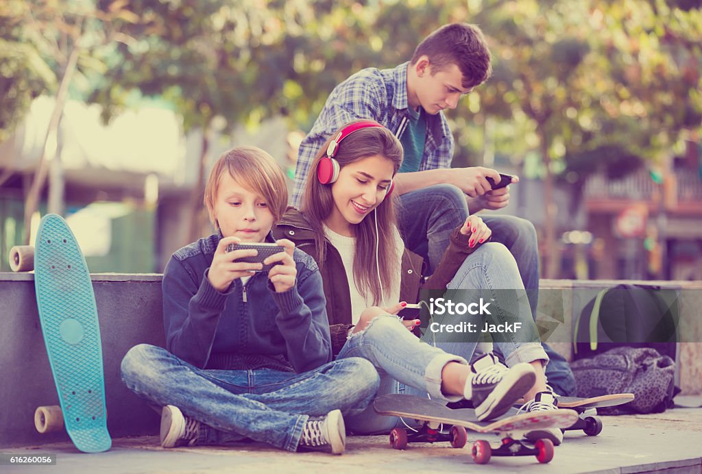 Three teenagers with phones outdoors Group of ordinary teenagers in casual relaxing with mobile phones outdoor. Focus on girl Teenager Stock Photo