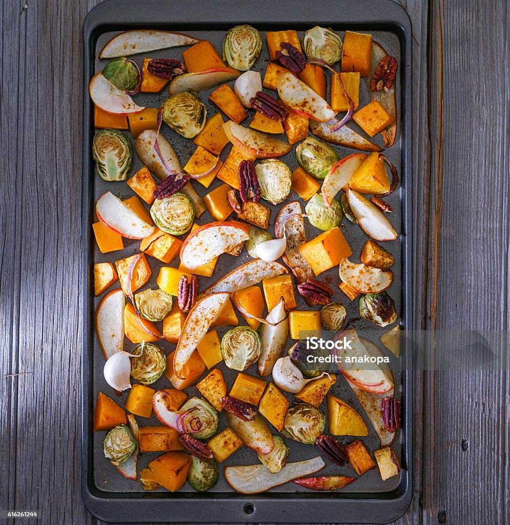Roasted cut vegetables and fruit on a baking sheet. Roasted root vegetables on a baking sheet: sweet potato, butternut squash, brussels sprouts, apple, pecans and pear. Toning. Healthy eating concept. Roasted Stock Photo
