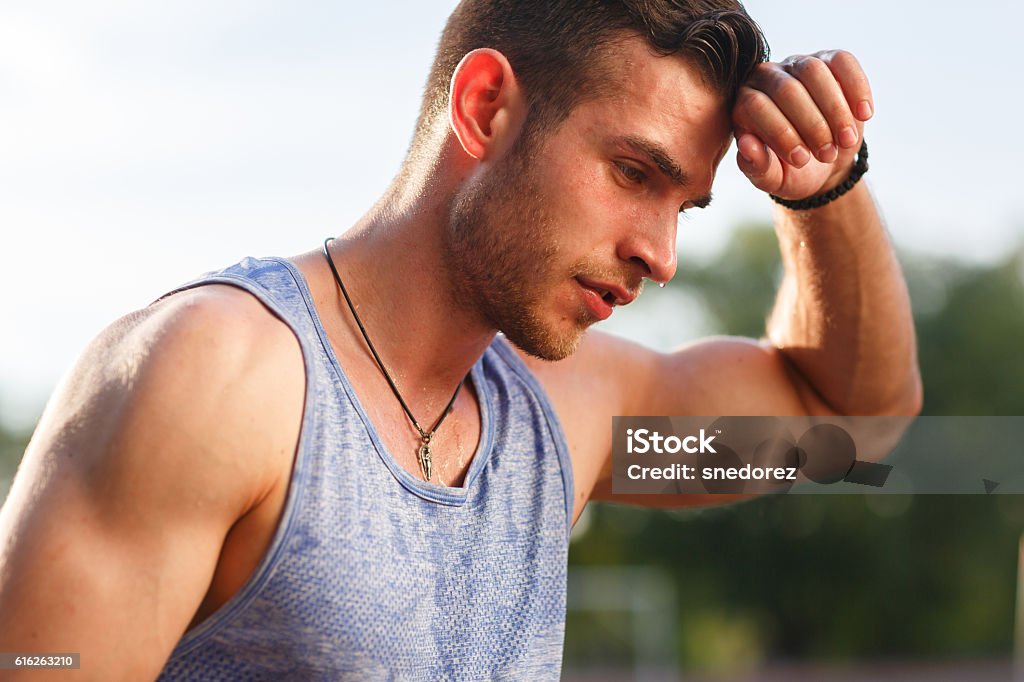 Tired wet athletic man wiping sweat his hand Tired wet athletic man in sports blue t-shirt wiping sweat his hand on nature background Sweat Stock Photo