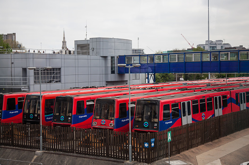 London, England - April 23, 2015: DLR TfL Train Depot next to Docklands. Five trains lined up next to the depot building. A blue foot bridge goes from the depot to the station
