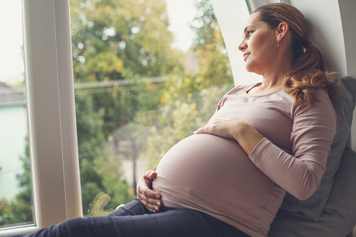 Pregnant woman holding her belly, looking through window