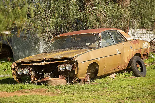 Old rusted car body and other car parts in a rural paddock