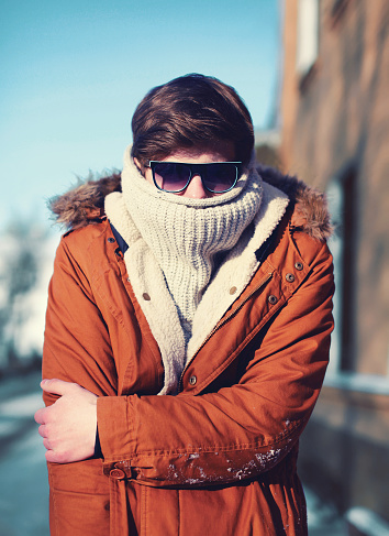 Fashion portrait hipster man freezes hides his head and warms body in winter city