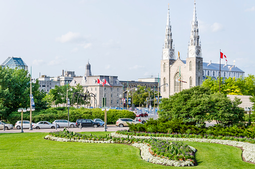 Ottawa, Canada - July 24, 2014: Notre-Dame Cathedral roman catholic Basilica with green trees and park with flags