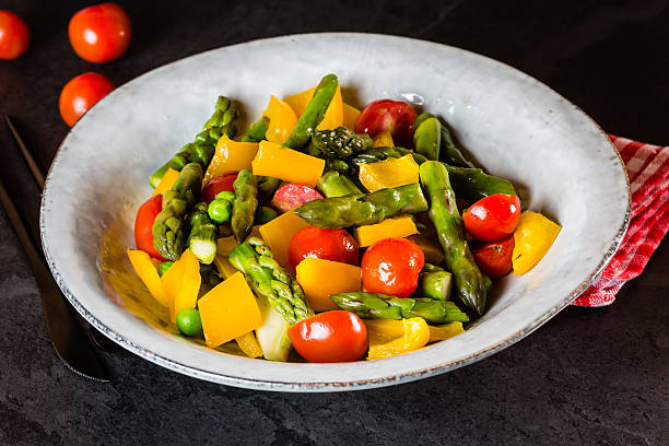 Vegetarian salad with asparagus, cherry tomatoes, bell pepper, slate background Mediterranean vegetarian salad. Vegan salad with asparagus, cherry tomatoes, yellow bell pepper on gray plate on black slate stone background. Vegetarian or healthy food. Top view asparagus organic dinner close to stock pictures, royalty-free photos & images