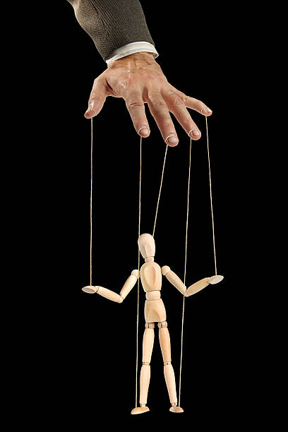 female hand with a puppet of a man in a black business suit on a pink background, manipulation and control concept