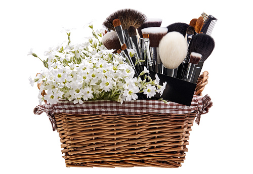 Makeup brushes set in crib with flowers. Chickweed. Isolated. White background.