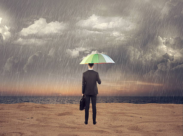 istock Businessman standing under an umbrella at beach 616895402