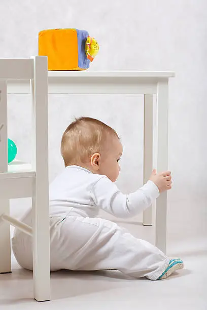 A baby of eight months old is making some activities on a gray background.
