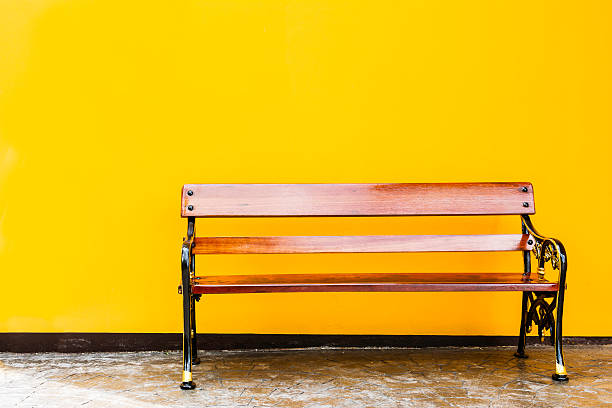 istock wood park bench in front of yellow wall. 616902606