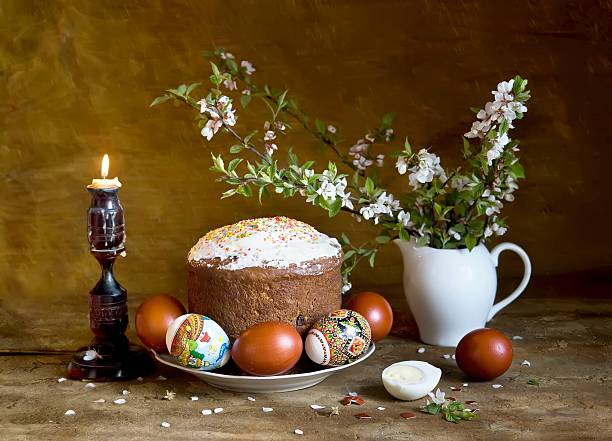 Paska (traditional Ukrainian Easter cake) and Easter eggs Paska (traditional Ukrainian Easter cake) and Easter eggs on a plate, beside burning candle and blooming cherry branches orthodox church easter stock pictures, royalty-free photos & images