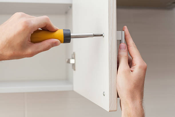 The worker sets a new handle on the white cabinet The worker sets a new handle on the white cabinet with a screwdriver disassembling stock pictures, royalty-free photos & images