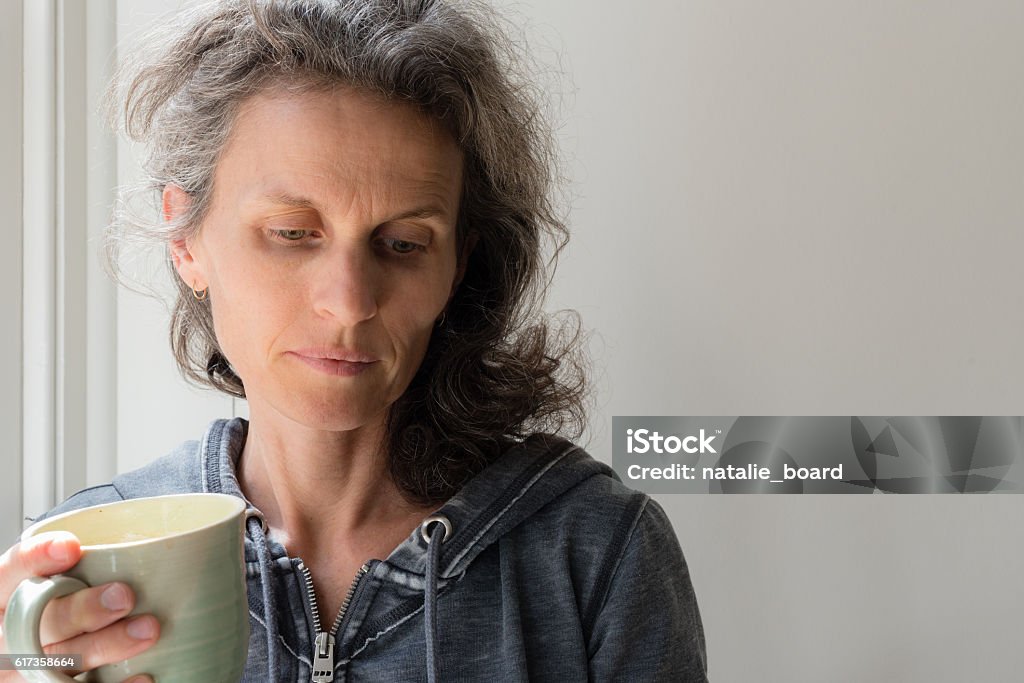 Middle aged woman with green cup Middle aged woman with grey hair holding green cup and looking pensive (selective focus) Tired Stock Photo