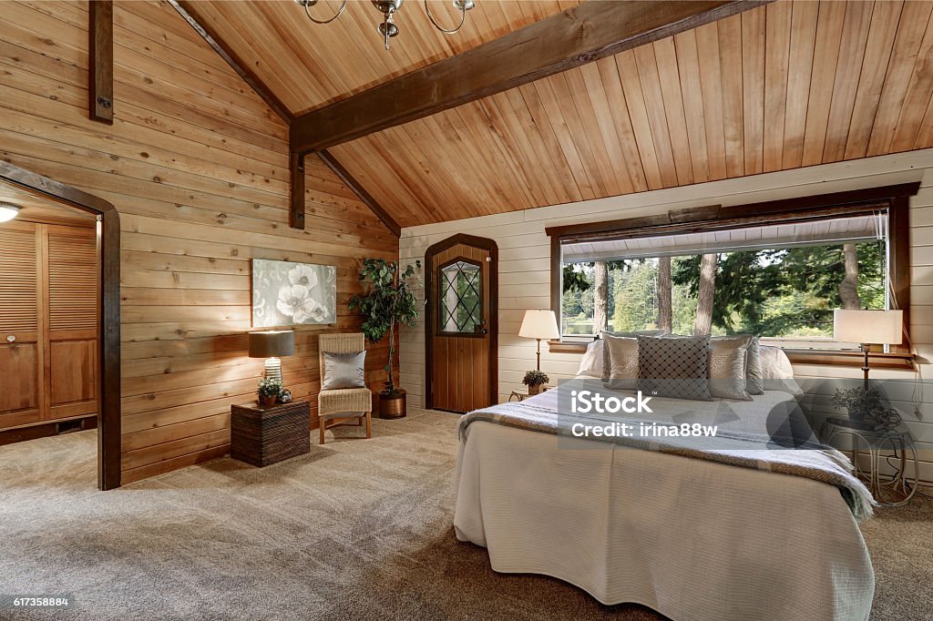 Wooden bedroom interior with high beamed ceiling Wooden bedroom interior with high beamed ceiling, grey carpet floor and large bed with neatly arranged pillows.  Northwest, USA Cottage Stock Photo