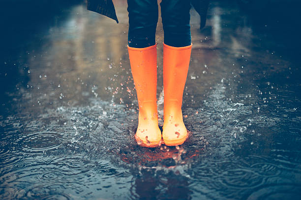 Feeling protected in her boots. Close-up of woman in orange rubber boots jumping on the puddle puddle photos stock pictures, royalty-free photos & images